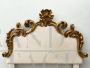 Antique bed headboard upholstered in white fabric and carved with gold leaf